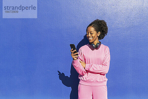 Glückliche Frau  die an einem sonnigen Tag ihr Smartphone vor der Wand benutzt