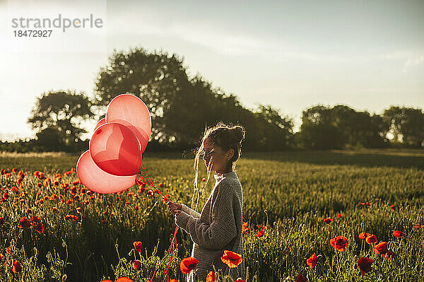 Mädchen hält Luftballons inmitten von Mohnblumen bei Sonnenuntergang