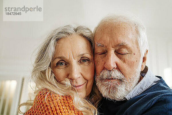 Smiling senior woman with man embracing each other at home