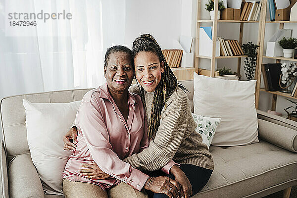Lächelnde Mutter und Tochter sitzen zu Hause auf dem Sofa