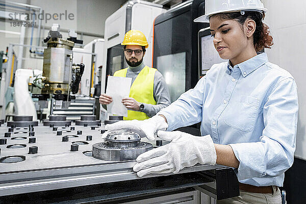 Lächelnde Geschäftsfrau  die in der Fabrik mit Maschinenteilen arbeitet