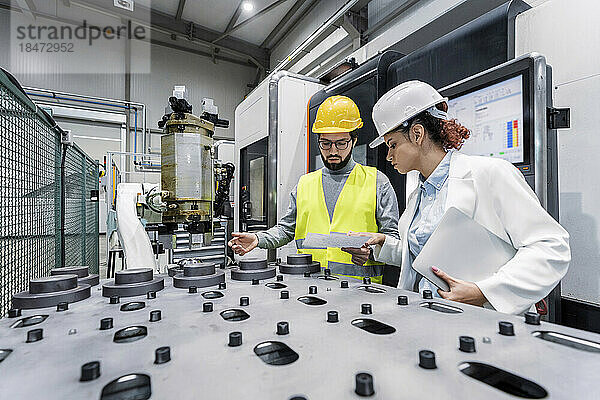 Engineer with colleague analyzing machine parts in factory