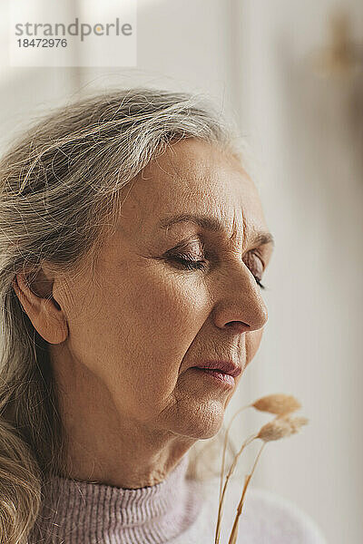 Ältere Frau mit geschlossenen Augen und trockener Pflanze zu Hause