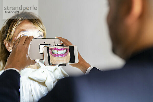 Geschäftsmann fotografiert mit Vergrößerungsgerät das Lächeln eines Kollegen per Smartphone