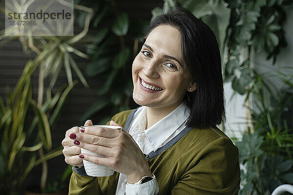 Glückliche Frau mit Kaffeetasse vor Pflanzen