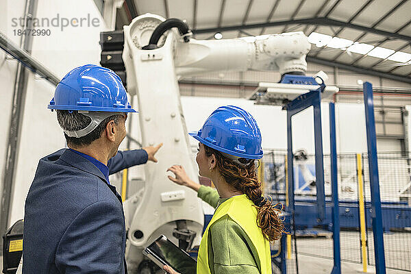 Ingenieure mit Schutzhelm diskutieren vor dem Roboterarm in der Fabrik