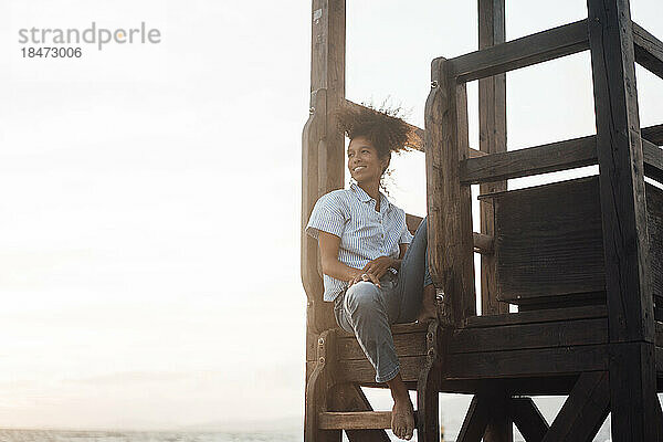 Junge Frau sitzt bei Sonnenuntergang auf Rettungsschwimmerhütte