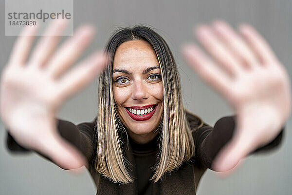 Happy woman making finger frame against gray background