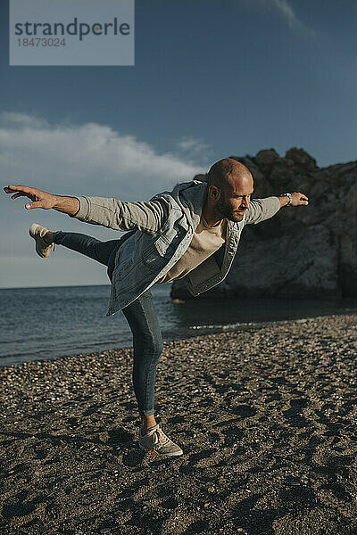 Mann balanciert auf einem Bein am Strand