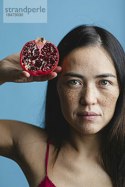 Frau mit Sommersprossen im Gesicht hält Granatapfelfrucht in der Hand