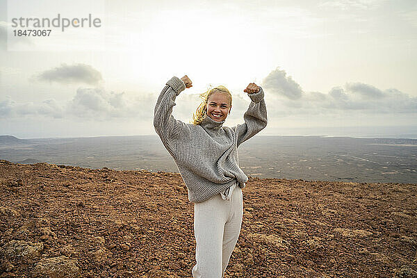 Glückliche junge Frau  die auf dem Berg steht und ihre Muskeln spielen lässt