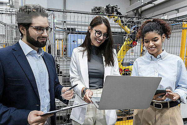 Glückliche Geschäftsfrau  die Laptop mit Kollegen in der Fabrik teilt