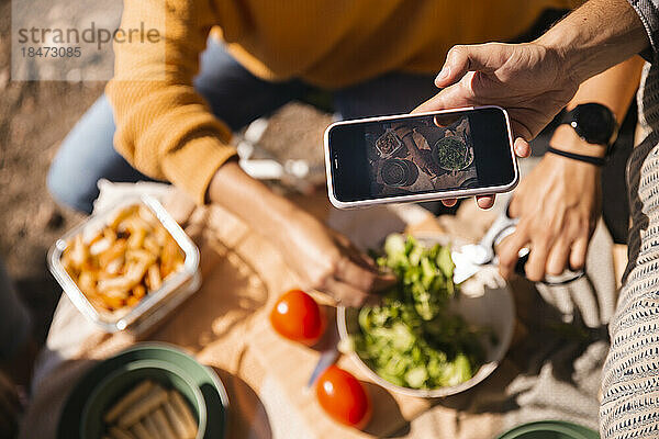Hand eines Mannes  der eine Mahlzeit per Smartphone fotografiert