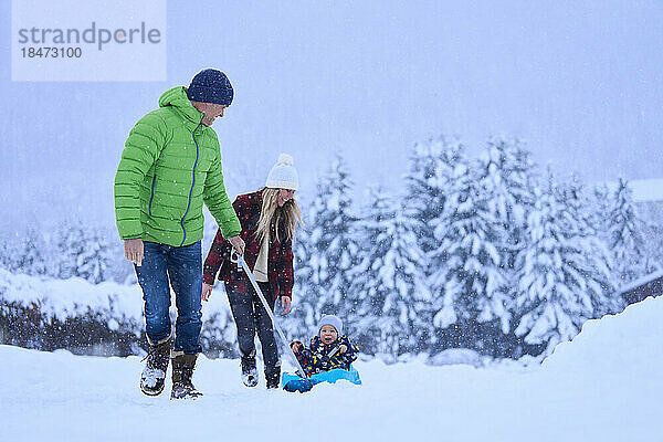 Mutter und Vater mit Sohn sitzen auf Schlitten im Schnee