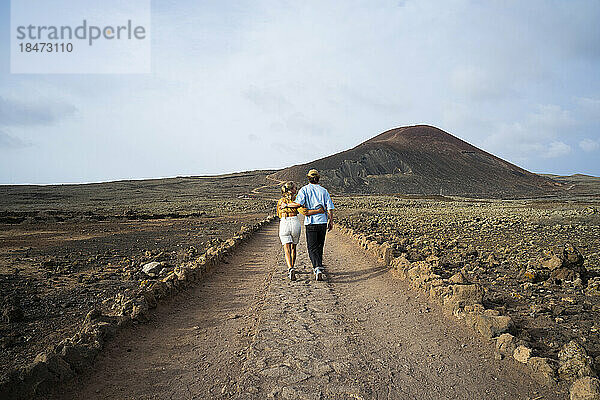 Junges Paar läuft auf unbefestigter Straße in vulkanischer Landschaft