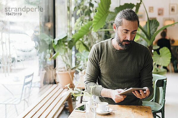 Reifer Mann sitzt mit Tablet-PC am Tisch im Café