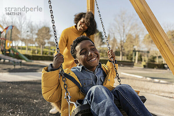 Happy mother pushing son on swing at playground