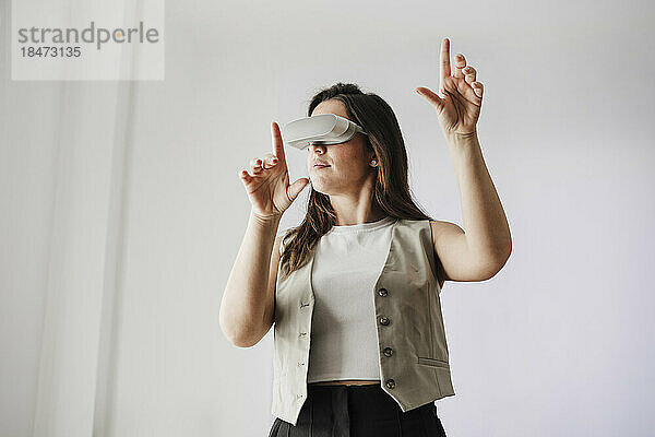 Geschäftsfrau mit VR-Brille gestikuliert vor weißer Wand