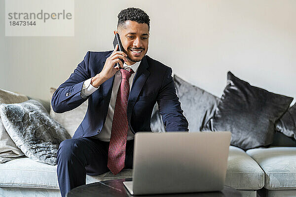 Happy businessman talking through smart phone sitting on couch