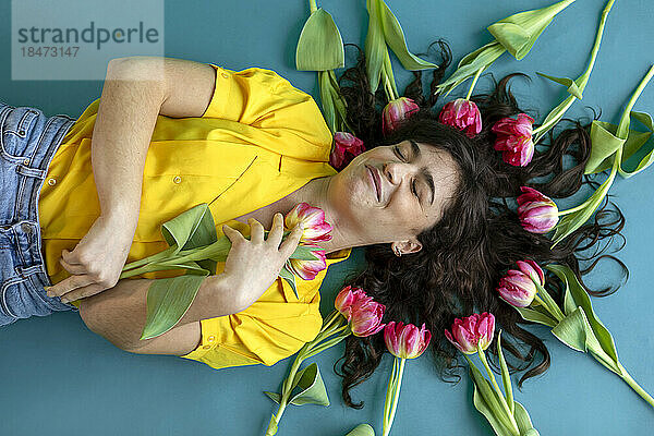 Woman with eyes closed lying down amidst tulips on green background