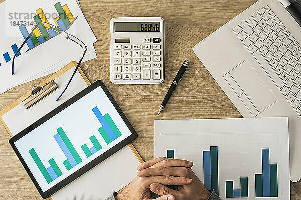 Hands of businessman with calculator and graphs on table