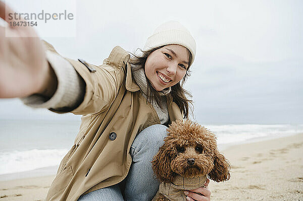 Glückliche Frau macht Selfie mit Hund am Strand