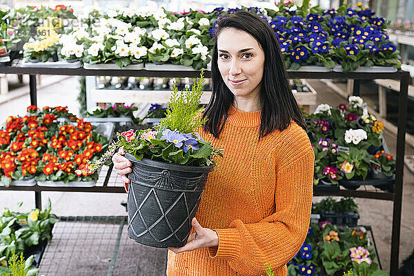 Lächelnde Frau mit blühenden Pflanzen  die im Gewächshaus steht