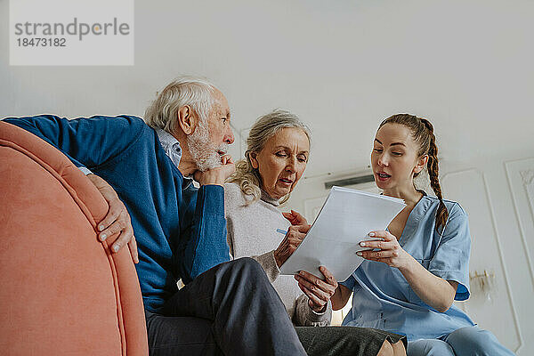 Pflegekraft hilft älteren Patienten beim Unterschreiben des Dokuments zu Hause