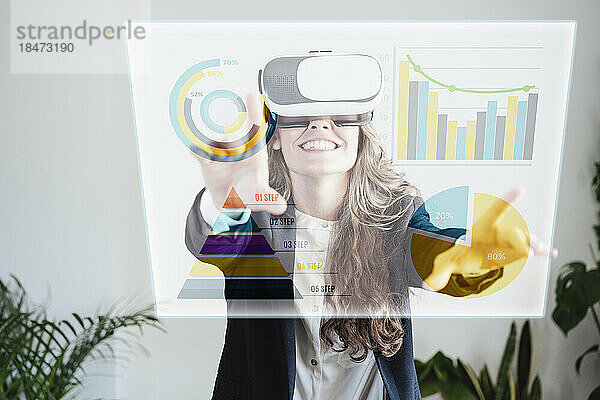 Glückliche Geschäftsfrau trägt eine VR-Brille und untersucht Diagramme und Kreisdiagramme