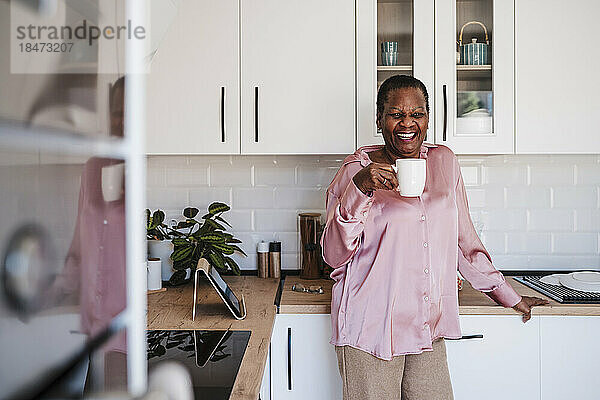 Glückliche Frau hält Tasse in der Küche zu Hause