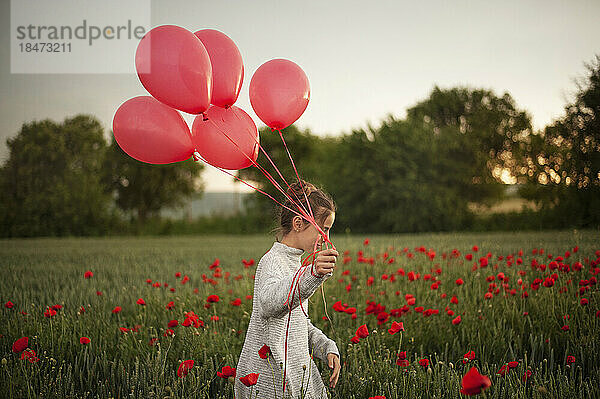 Mädchen läuft mit Luftballons im Mohnfeld