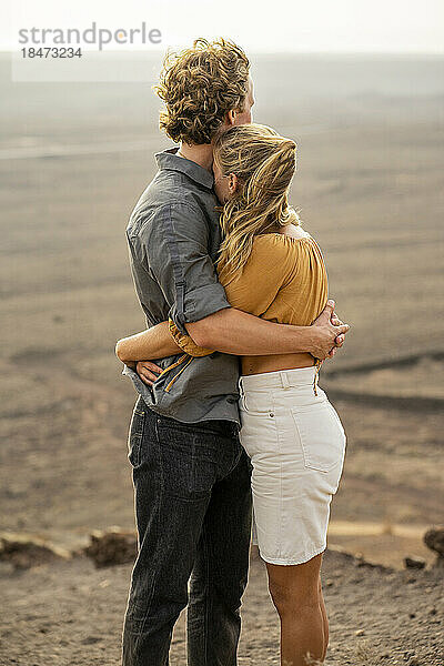 Junger Mann umarmt Freundin  die auf dem Berg steht