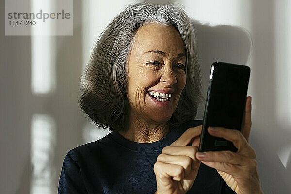 Lächelnde reife Frau benutzt Smartphone vor der Wand