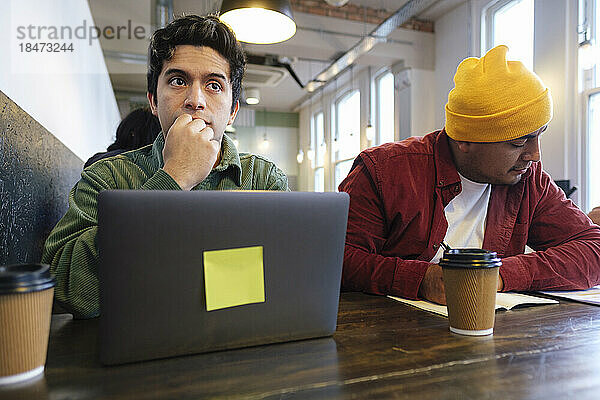 Nachdenklicher Freiberufler mit Bruder schreibt im Café auf Notizblock
