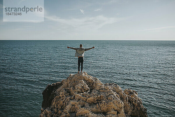Sorgloser Mann steht mit ausgestreckten Armen auf einem Felsen vor dem Meer