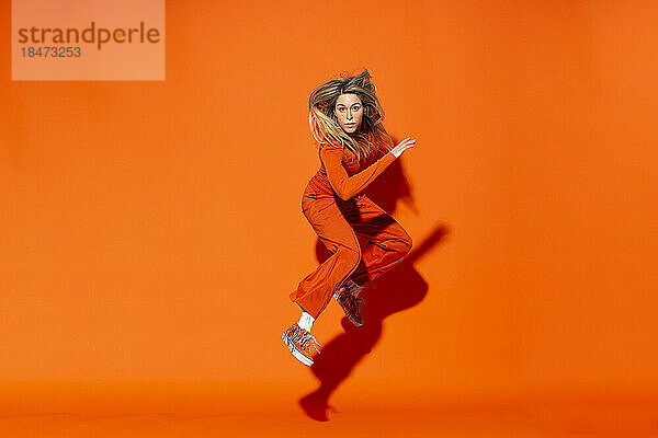 Aktive Frau springt vor orangefarbenem Hintergrund