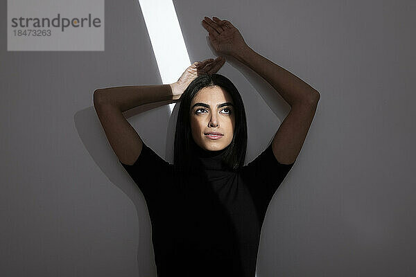Nachdenkliche junge Frau mit Licht im Gesicht vor der Wand