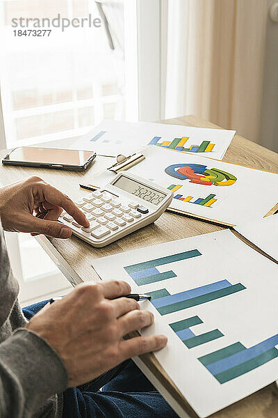Hände eines Geschäftsmannes  der im Büro Diagramme untersucht und Berechnungen durchführt
