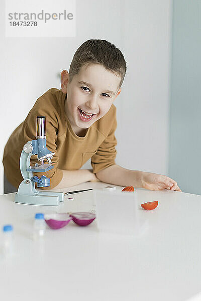 Fröhlicher Junge lehnt am Tisch mit Mikroskop