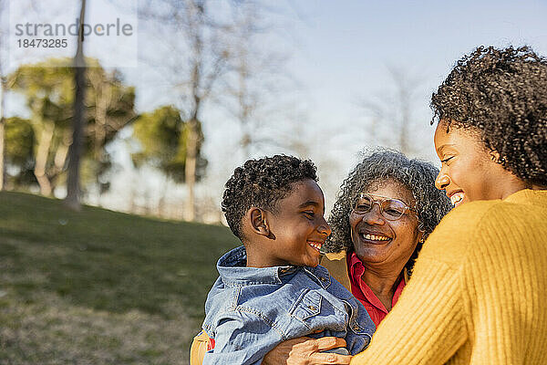 Glückliche ältere Frau trägt Enkel und hat Spaß mit Mutter im Park