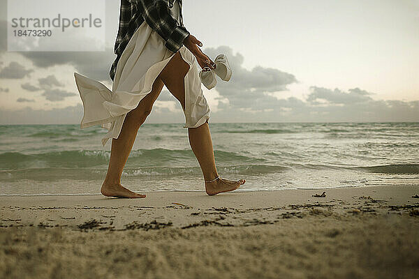Frau läuft barfuß auf Sand in Ufernähe am Strand