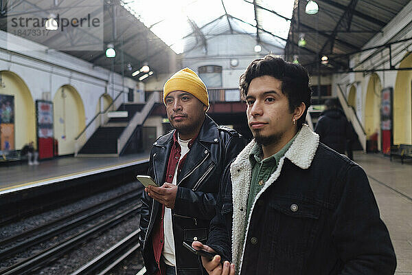 Brüder mit Smartphones stehen am Bahnsteig