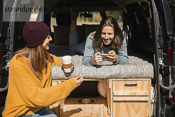 Frau spricht mit lächelndem Freund über Smartphone  das im Wohnmobil liegt