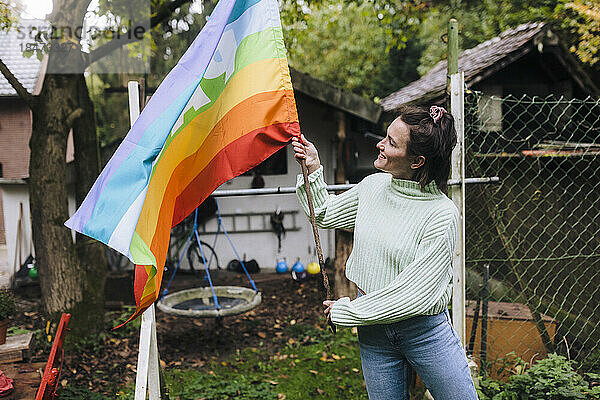 Glückliche Frau steht mit Regenbogenfahne im Hinterhof