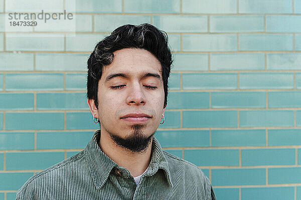 Man with eyes closed in front of turquoise brick wall