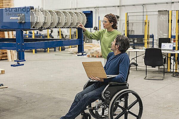 Ingenieur untersucht Maschinenteil mit Kollege im Rollstuhl im Büro