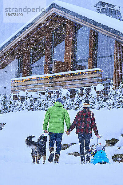 Eltern mit Sohn und Hund gehen im Schnee spazieren