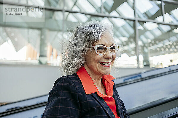 Glückliche Geschäftsfrau mit Brille auf Rolltreppe am Bahnhof