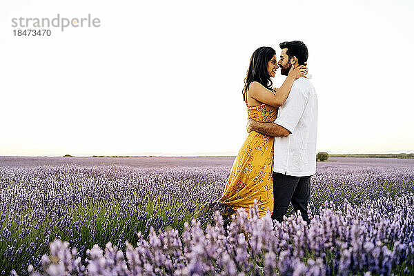 Smiling young woman embracing man standing in lavender field