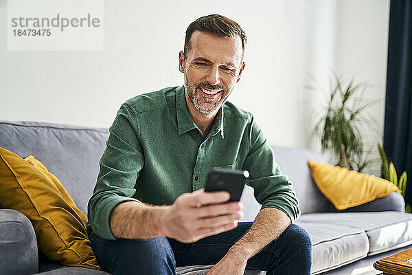 Cheerful man sitting on couch using smartphone